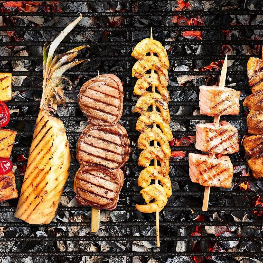 Ananas, médaillons de viande, crevettes et saumon en brochettes sur la grille au-dessus des braises